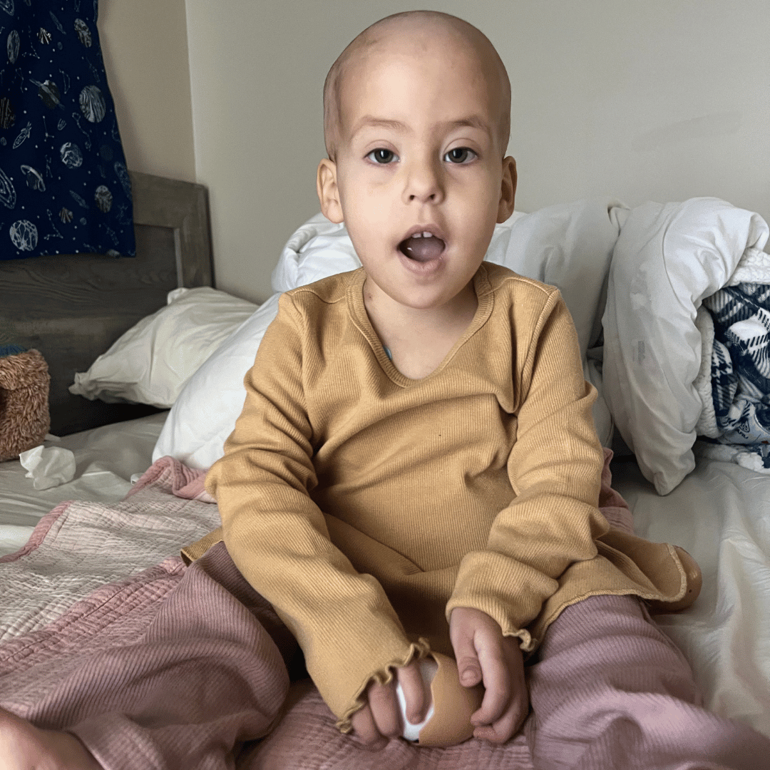 All-Star Nora sitting in her hospital bed with a pink blanket on