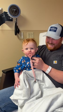 All-Star Lydia looking at the camera while sitting on her dads lap in the hospital. 