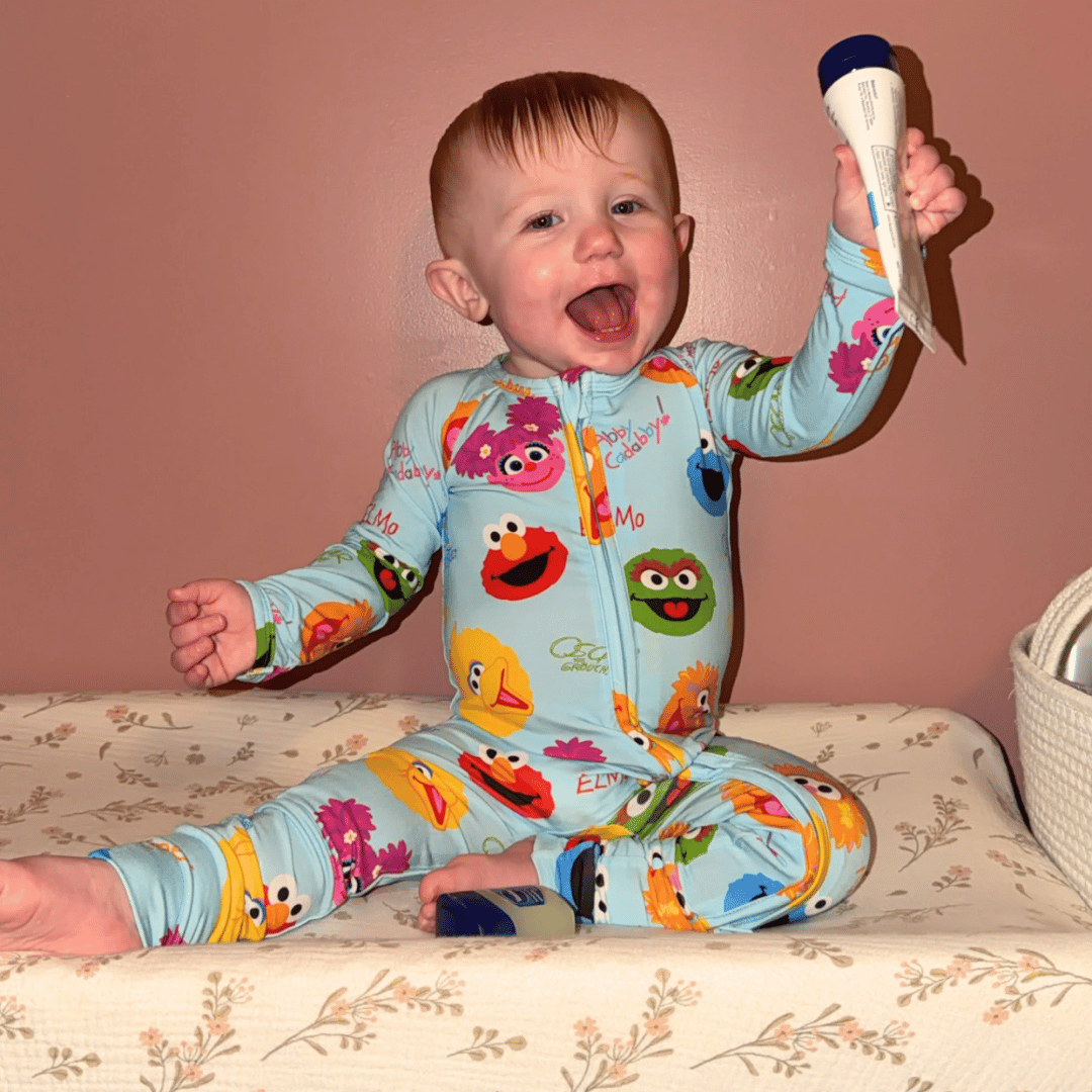 A little 1-year-old named Lydia wearing Sesame Street pajamas, smiling while holding up a tube of cream