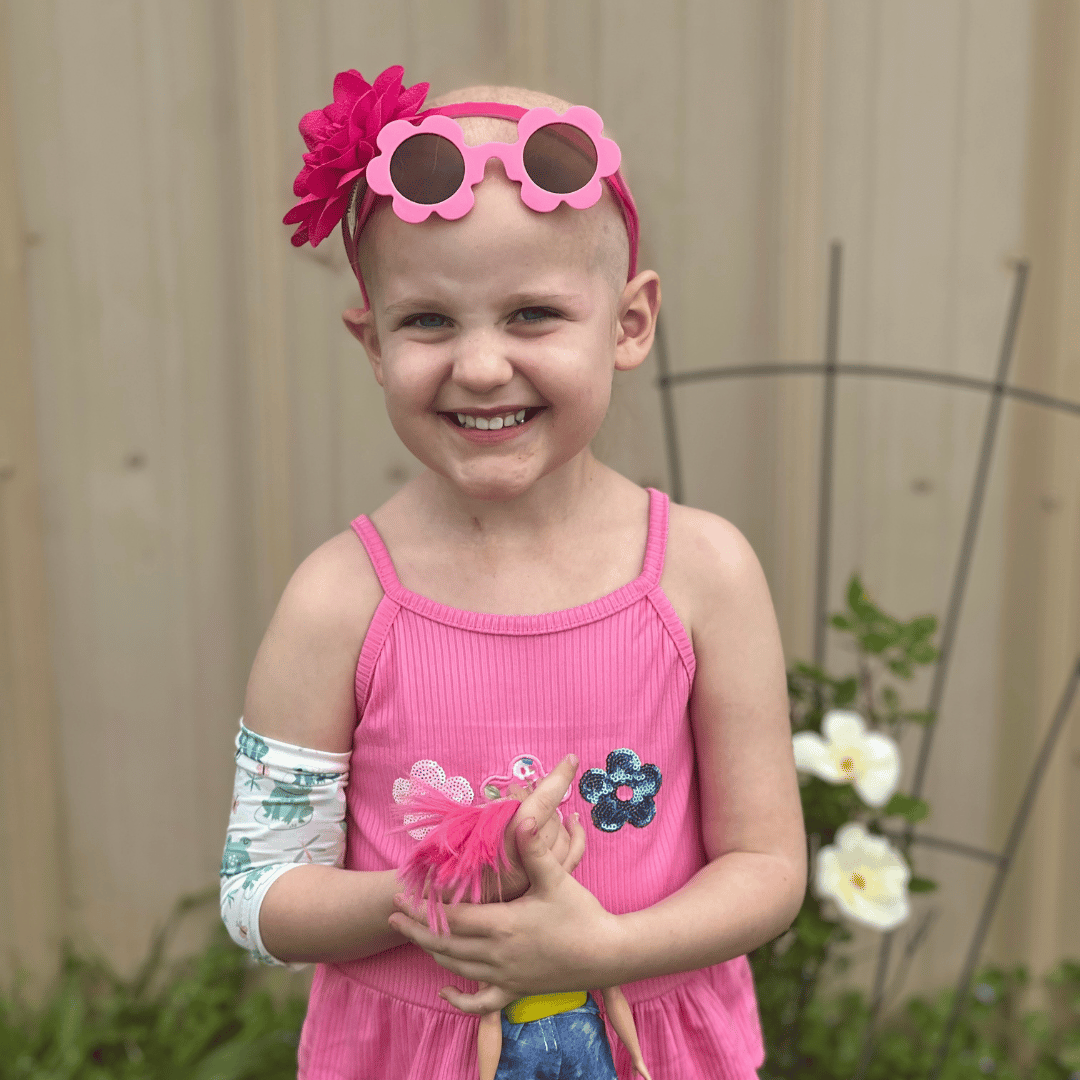 A little girl named Scarlett wearing pink sunglasses, a pink dress holding a doll