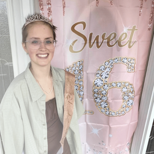 All-Star Ella with a birthday sash and a birthday crown standing in front of a Sweet 16 banner on the door