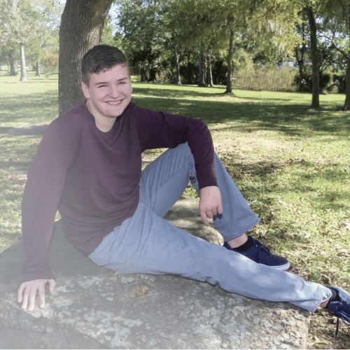 All-Star Lance sitting on a rock wearing a maroon shirt and grey pants