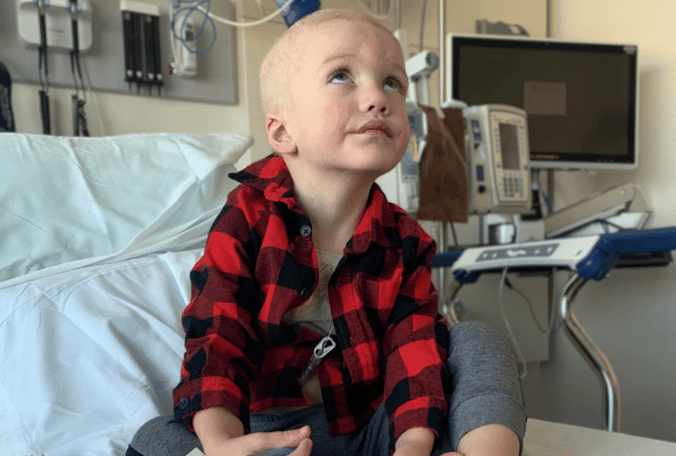 A little boy named Beau sitting in his hospital bed looking up while coloring.