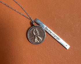 A necklace with a penny on it and a pendant that says "Be the change"