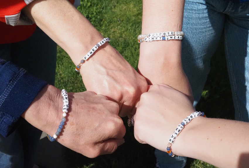 A group of Pinky Swear team members putting their hands in to show collaboration while wearing Pinky Swear bracelets.