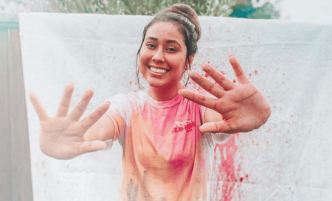 A college student with a brunette bun holding her two hands out towards the camera after getting paint thrown on her at a fundraising event