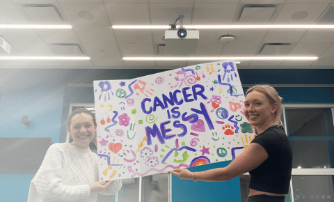 Two students holding up a Cancer is Messy sign in a classroom.