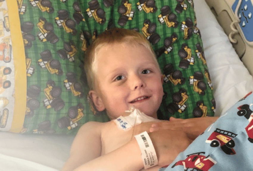 All-Star Eli lying in a hospital bed smiling with a tractor pillow behind him.