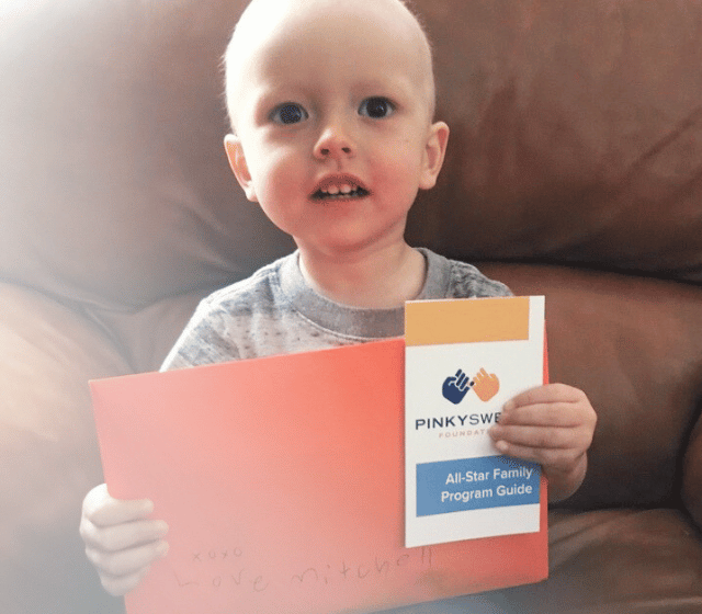 All-Star Max holding an orange envelope from Pinky Swear Foundation sitting on the ouchc