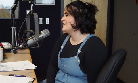 A woman in front of a radio mic smiling while telling her story about how Pinky Swear Foundation has helped her family during her childhood cancer diagnosis