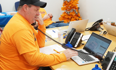 A volunteer at a Pinky Swear Radiothon answering the phone to take a donation while wearing a construction orange shirt.