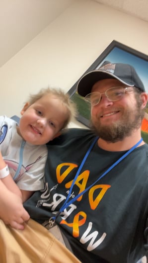 A little girl named Scarlett and her dad, James sitting together and smiling at the camera. 