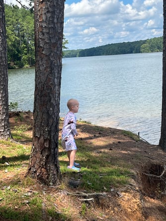 Scarlett outside standing next to a tree looking at a lake.