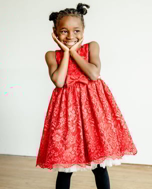 A young girl is a bright red dress named Za'nari who received support from Pinky Swear Foundation during her cancer diagnosis.