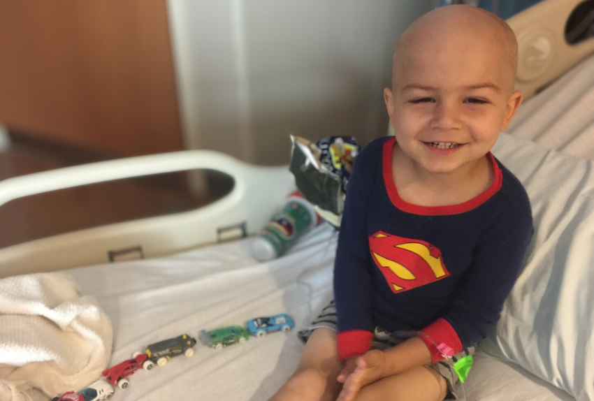 A little boy sitting on a hospital bed with a chain of cars next to him.
