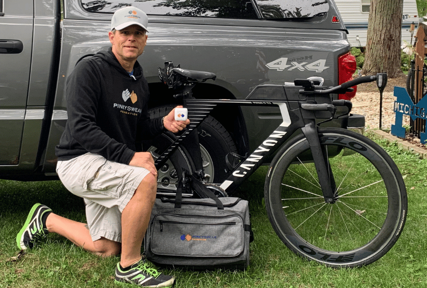 A person kneeling in front of their bike by their truck pointing out the Pinky Swear logos.