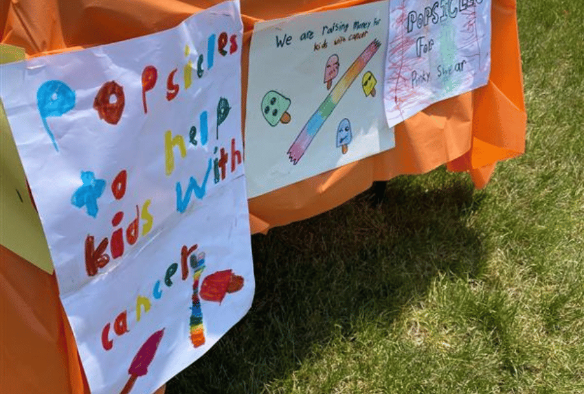 A sign hanging from a table that says Popsicles to help kids with cancer