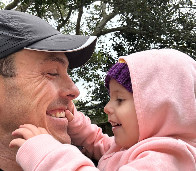 A girl facing cancer and her dad smiling at each other.
