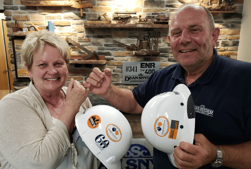 Jane and Don Snyder holding construction hats doing a Pinky Swear to show their support for the non-profit.