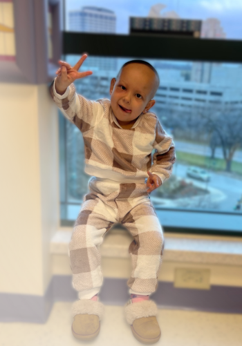 All-Star Kaylee throwing the piece sign while sitting on a window sill