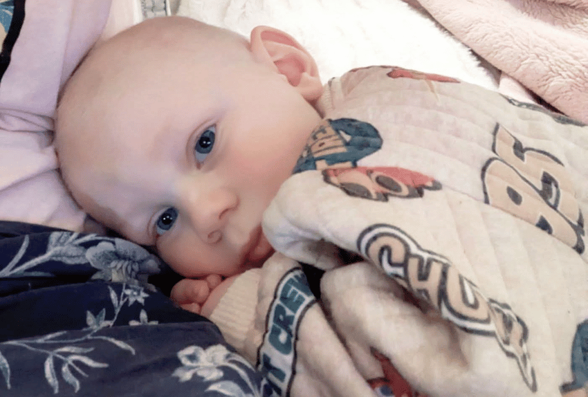 A little boy named Dublin lying down looking at the camera covered in a blanket.