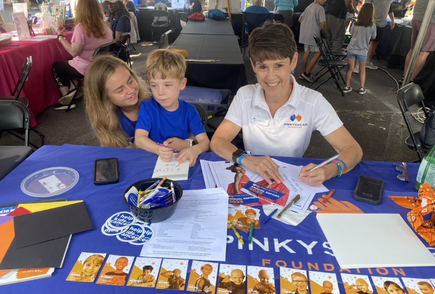Three people sitting at a table with Pinky Swear Foundation information on it