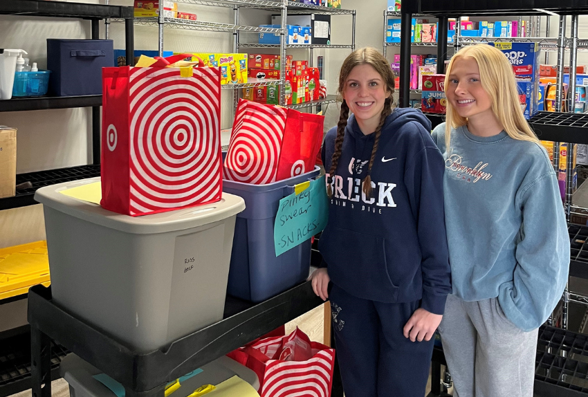 Two students standing next to a cart full of groceries to go to a pantry in the hospital for kids with cancer.