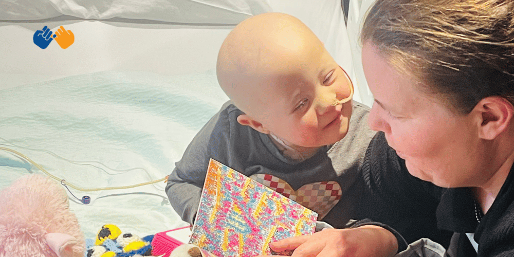 A little girl smiling at her mom while she reads to her in the hospital facing leukemia. Pinky Swear Foundation helped them financially during their cancer journey.