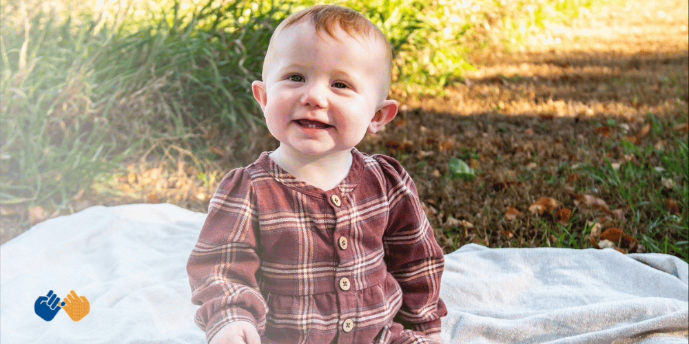 A little girl sitting on a blanket smiling at the camera