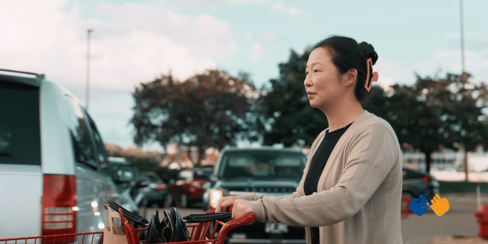 A woman pushing a cart through a grocery store parking lot.