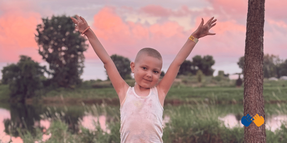 A girl named winnie holding both arms up in the air with a cotton candy sunset in the background